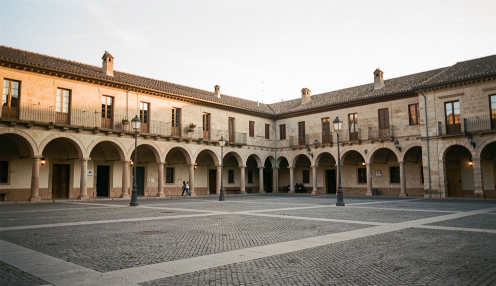 Plaza porticada de una ciudad castellana al atardecer, con soportales y tejados