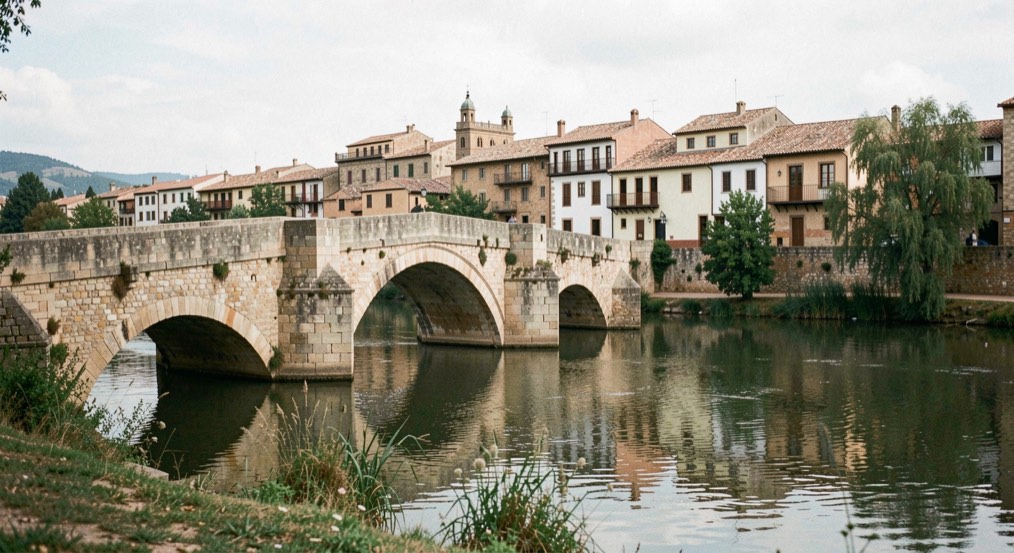 Río tranquilo con un puente de piedra antiguo y tejados históricos de una ciudad castellana al fondo